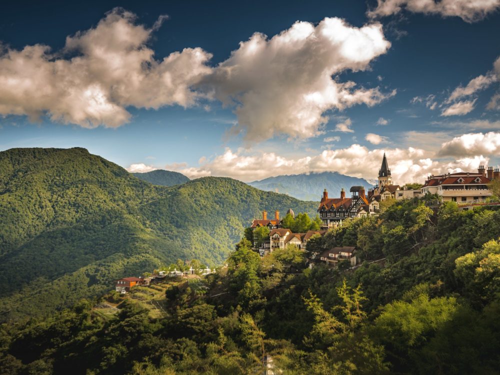 An aerial shot of a small village on the hill surrounded by forested mountains