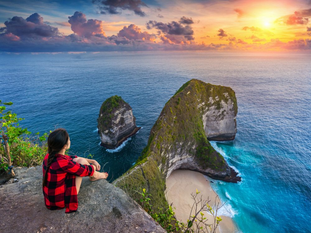 Woman sitting on cliff and looking at sunset at Kelingking Beach in Nusa penida island, Bali, Indonesia.